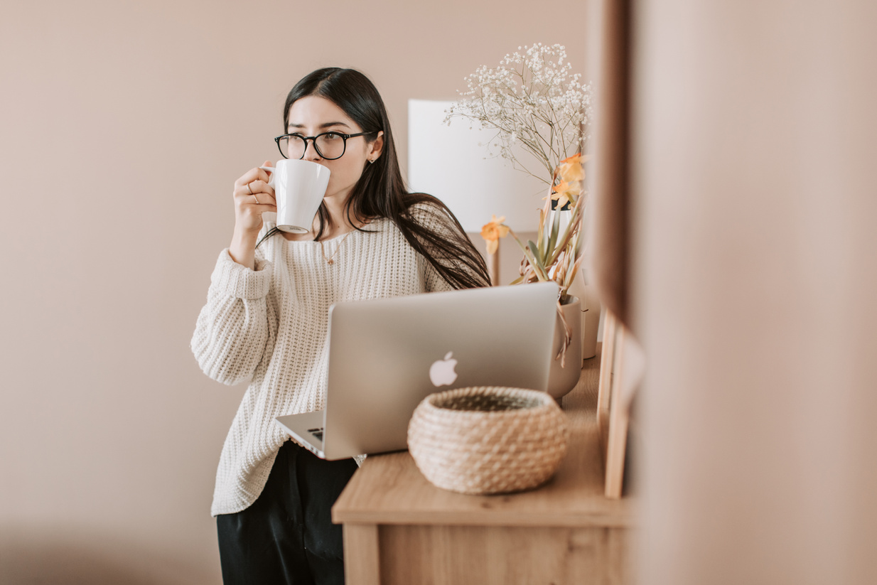 Woman Drinking Coffee WhilebStanding Near A Laptop